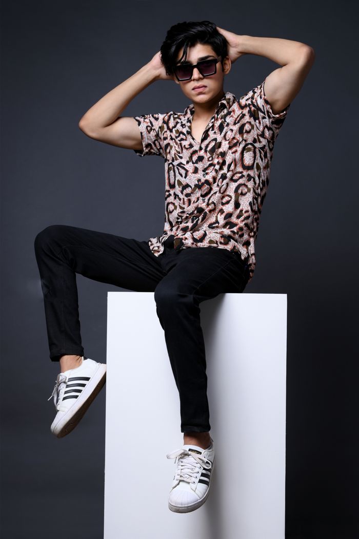 A fashionable young man poses in a studio wearing a printed shirt and sunglasses, exuding style and confidence.