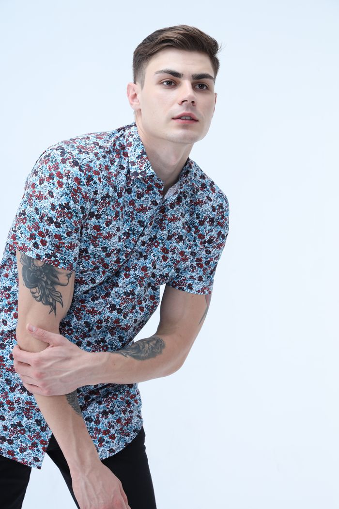 Caucasian man with stylish shirt and arm tattoo poses in studio. Perfect for fashion and lifestyle themes.